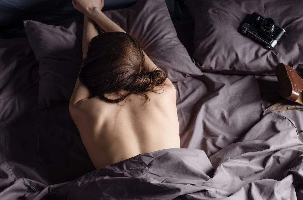 Young woman in bed covered by dark sheets.